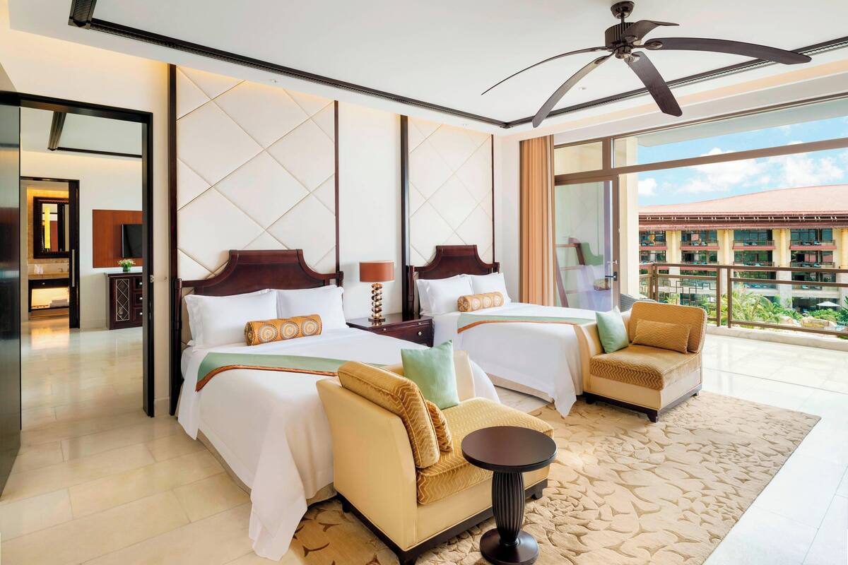Une chambre d’hôtel avec deux lits, un canapé, une petite table et un balcon donnant sur des immeubles.