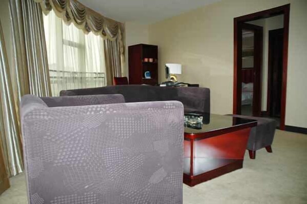 Una habitación de hotel con un sofá, una mesa de centro de vidrio, una estantería y una puerta.