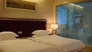 A hotel room with two beds, a headboard, a bedside table with a lamp, and a large window with blinds. - Guangzhou Tianyue Hotel (Guangzhou)