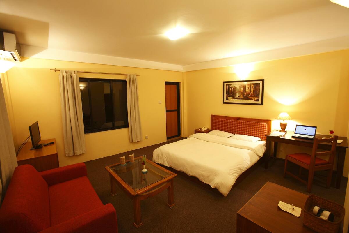 A hotel room with a bed, a desk with a laptop, a red sofa, and a small table.