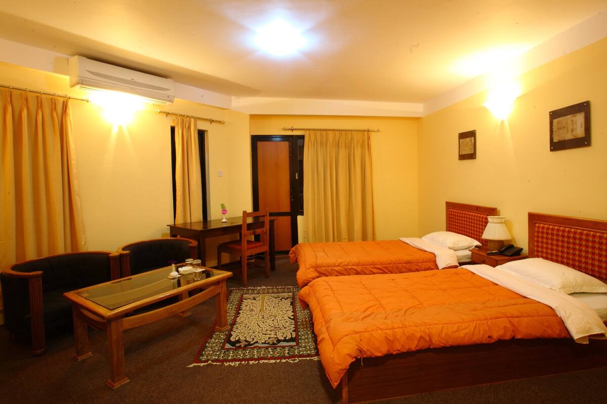 A hotel room with two beds, a desk, a chair, and an air conditioning unit.