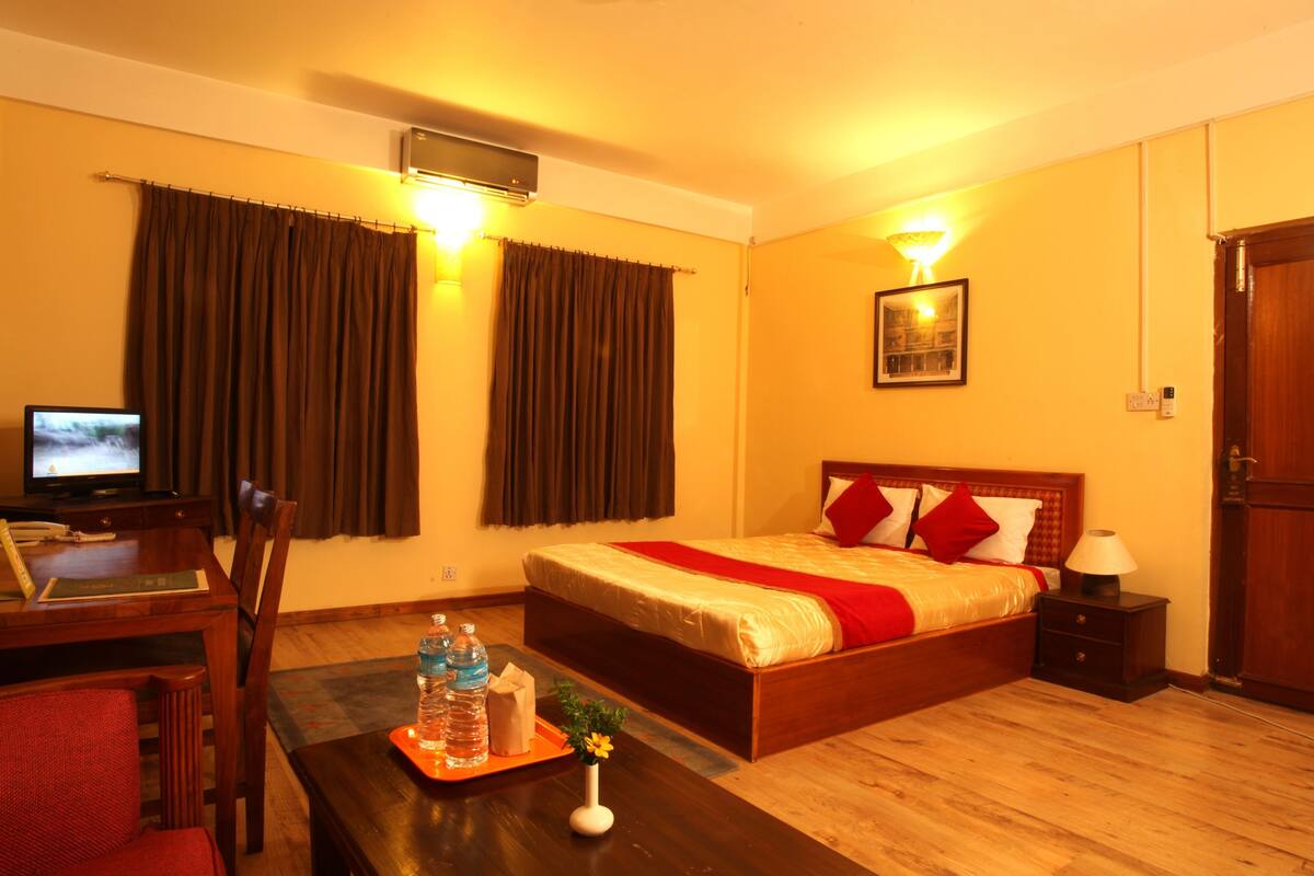 A hotel room with a wooden bed, a desk with a computer, a table with water bottles, and a lamp.