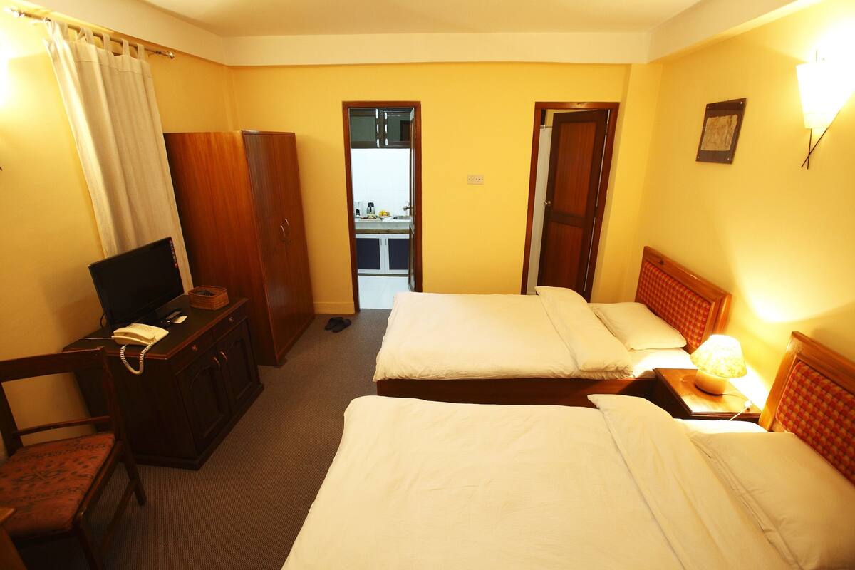 A hotel room with two beds, a desk with a telephone, a TV, and a wardrobe.