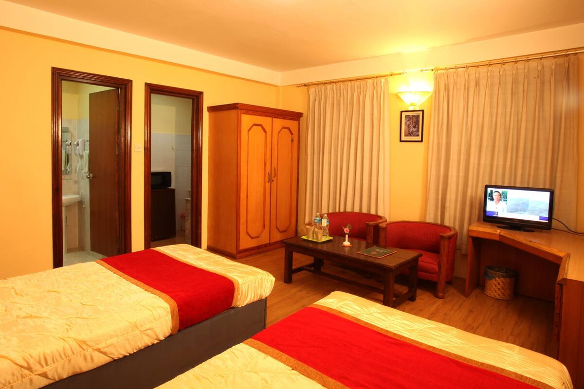 A hotel room with two beds, a desk, a chair, a television, and a wardrobe.