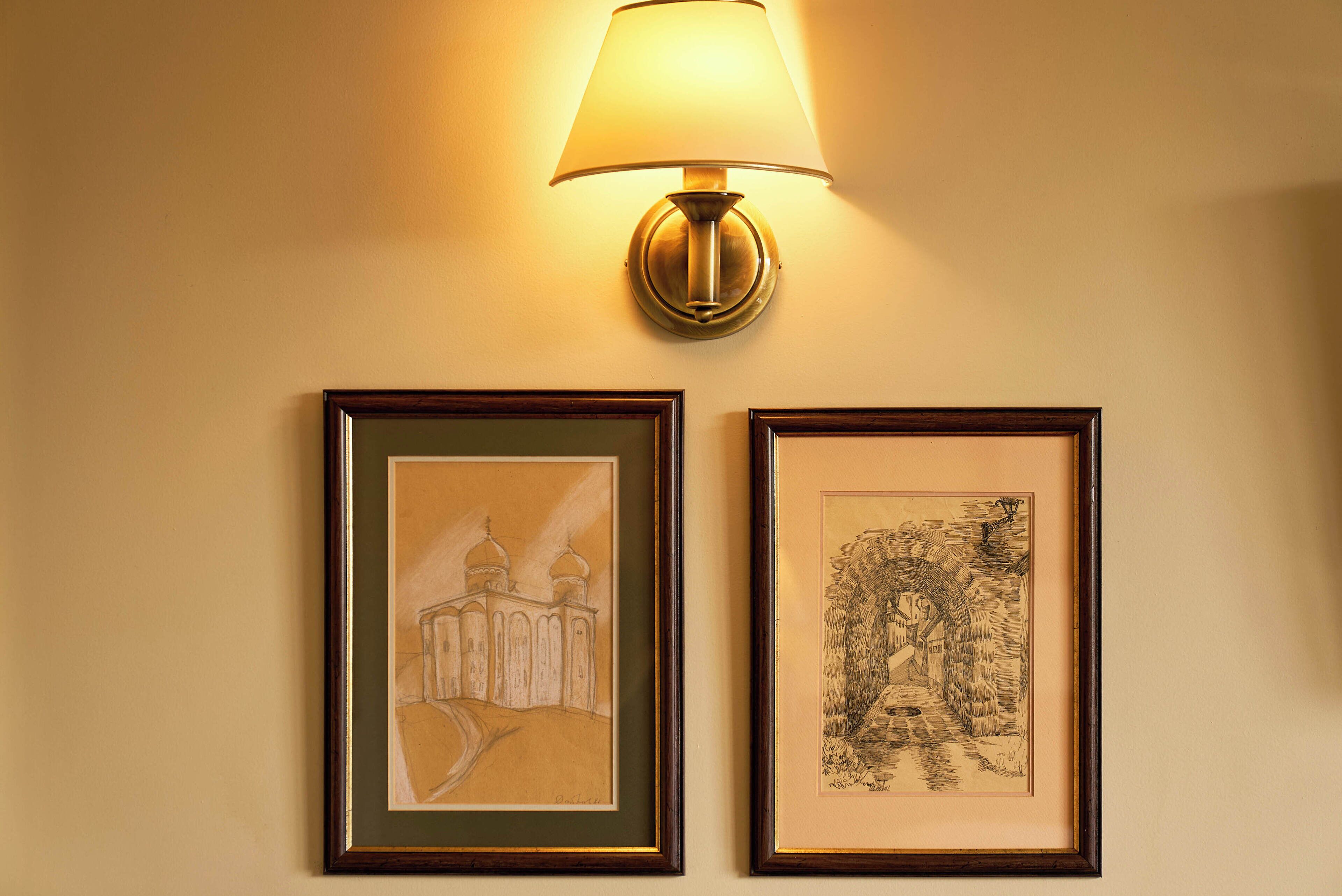 Twee kunstwerken in lijsten aan een muur, waarvan er één een gebouw met koepels toont en de andere een landschap met een brug.