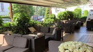 An outdoor seating area with wicker furniture, a glass table, and a vase of white flowers.