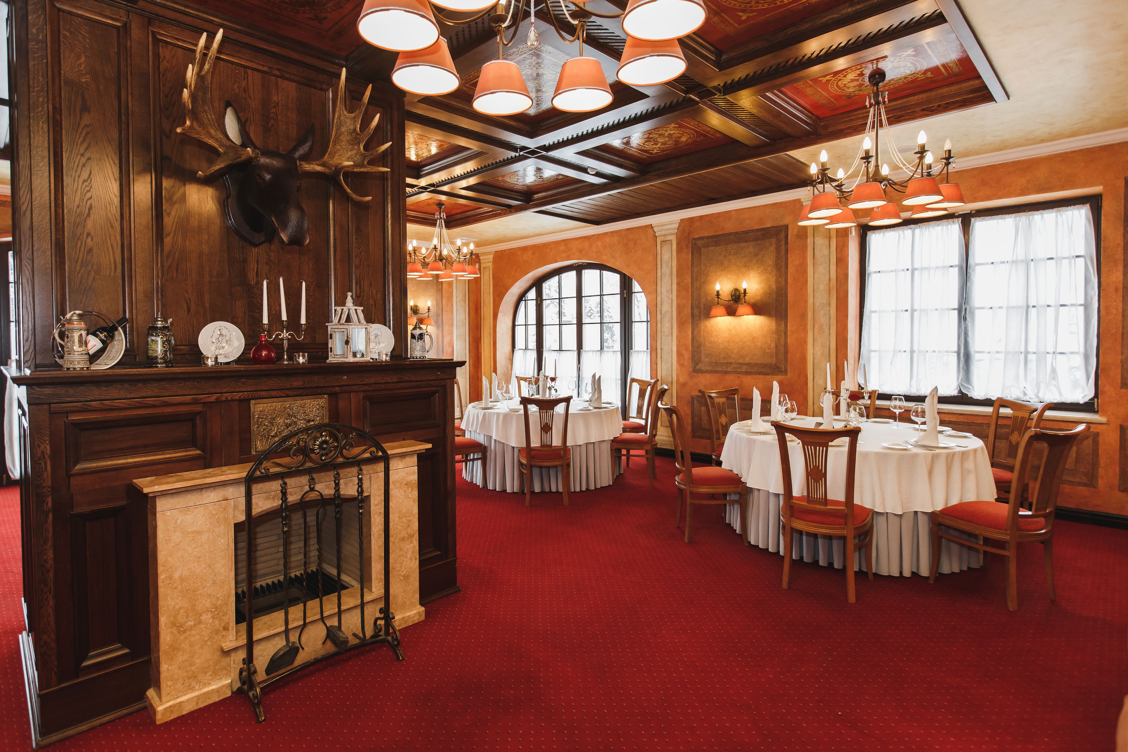 A dining area with round tables, wooden chairs, a fireplace, and chandeliers.