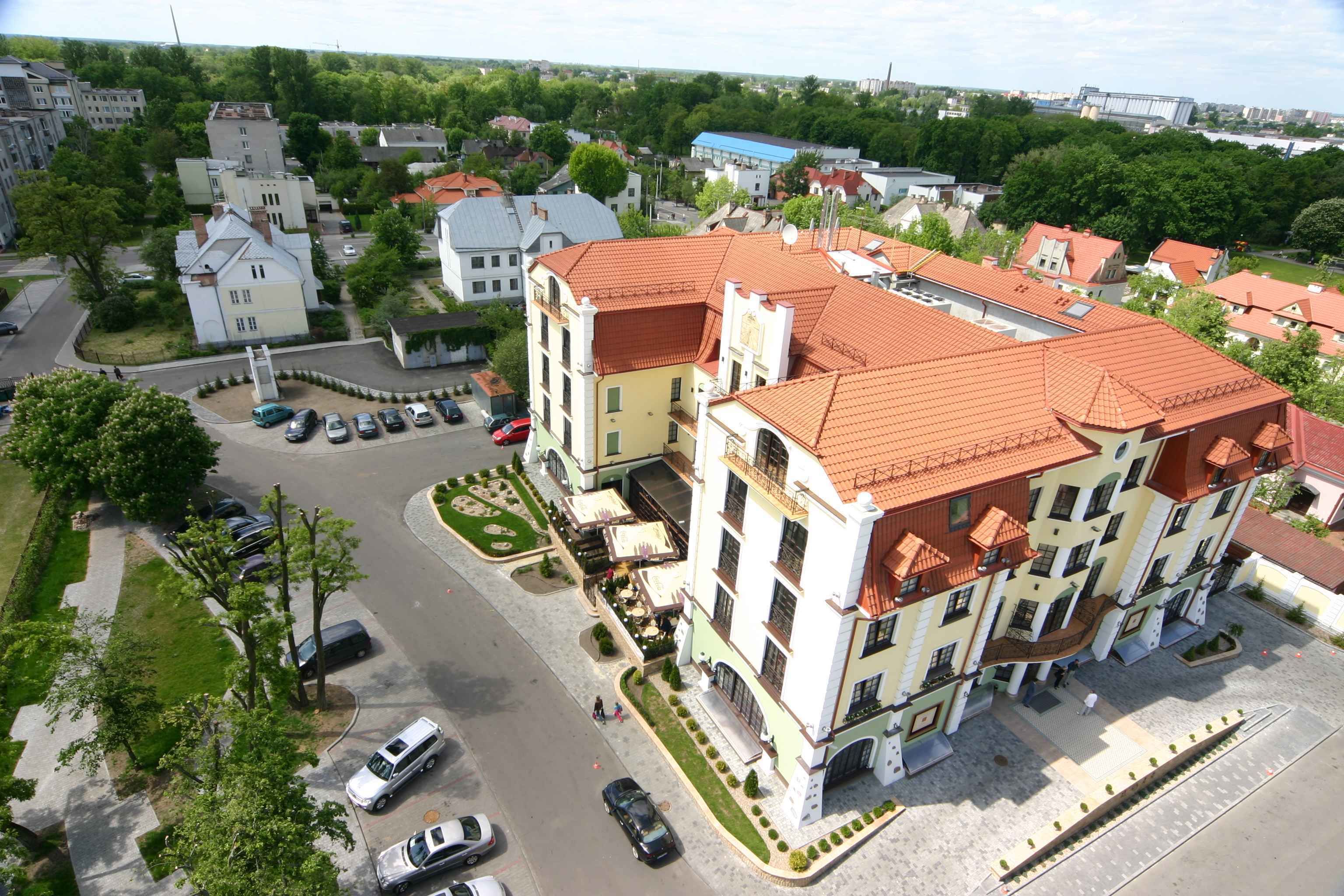 Un hôtel à plusieurs étages, doté d’un toit recouvert de tuiles rouges, d’une cour intérieure et d’un parking.