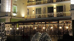 A multi-story building with balconies adorned with string lights, a green-lit entrance, and a decorative light installation in front.
