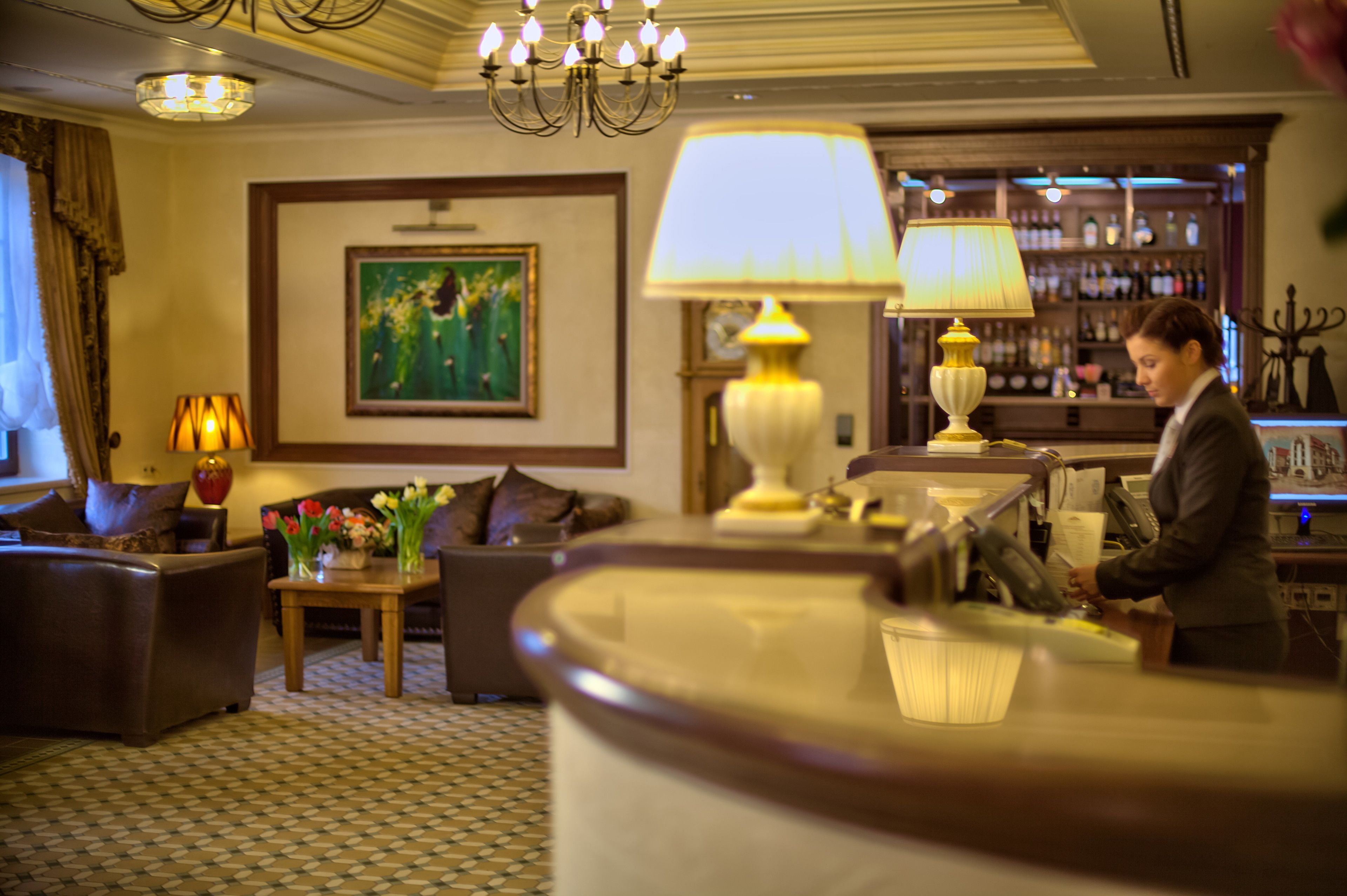 A hotel lobby with a bar area, sofas, a chandelier, and a painting on the wall.