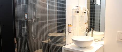 Un baño moderno con ducha de vidrio, lavabo blanco y un espejo grande.