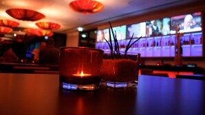 Un coin bar faiblement éclairé, avec une bougie et un récipient en verre posés sur une table.