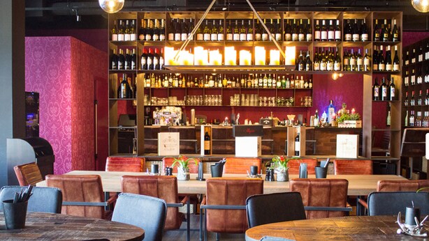 Un espace bar doté de plusieurs types de sièges et d’une étagère bien garnie de vins et de spiritueux.