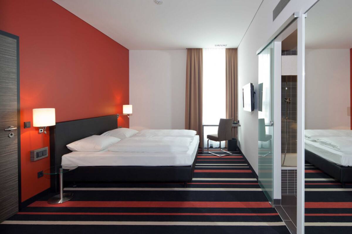 A hotel room with a large bed, a desk, a chair, a TV, and a shower area.