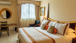 A hotel room with a large bed, a desk, a chair, a lamp, and a window with curtains. - Toscana Inn (Panama City)