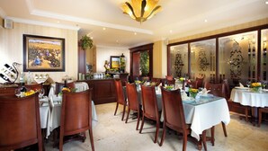 A dining area with tables set for a meal, chairs, a chandelier, and a large framed painting on the wall. - Toscana Inn (Panama City)