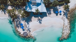 An aerial view of a beach resort with a large house, multiple lounge chairs, and umbrellas. - Siboney Beach Club (St. John's)