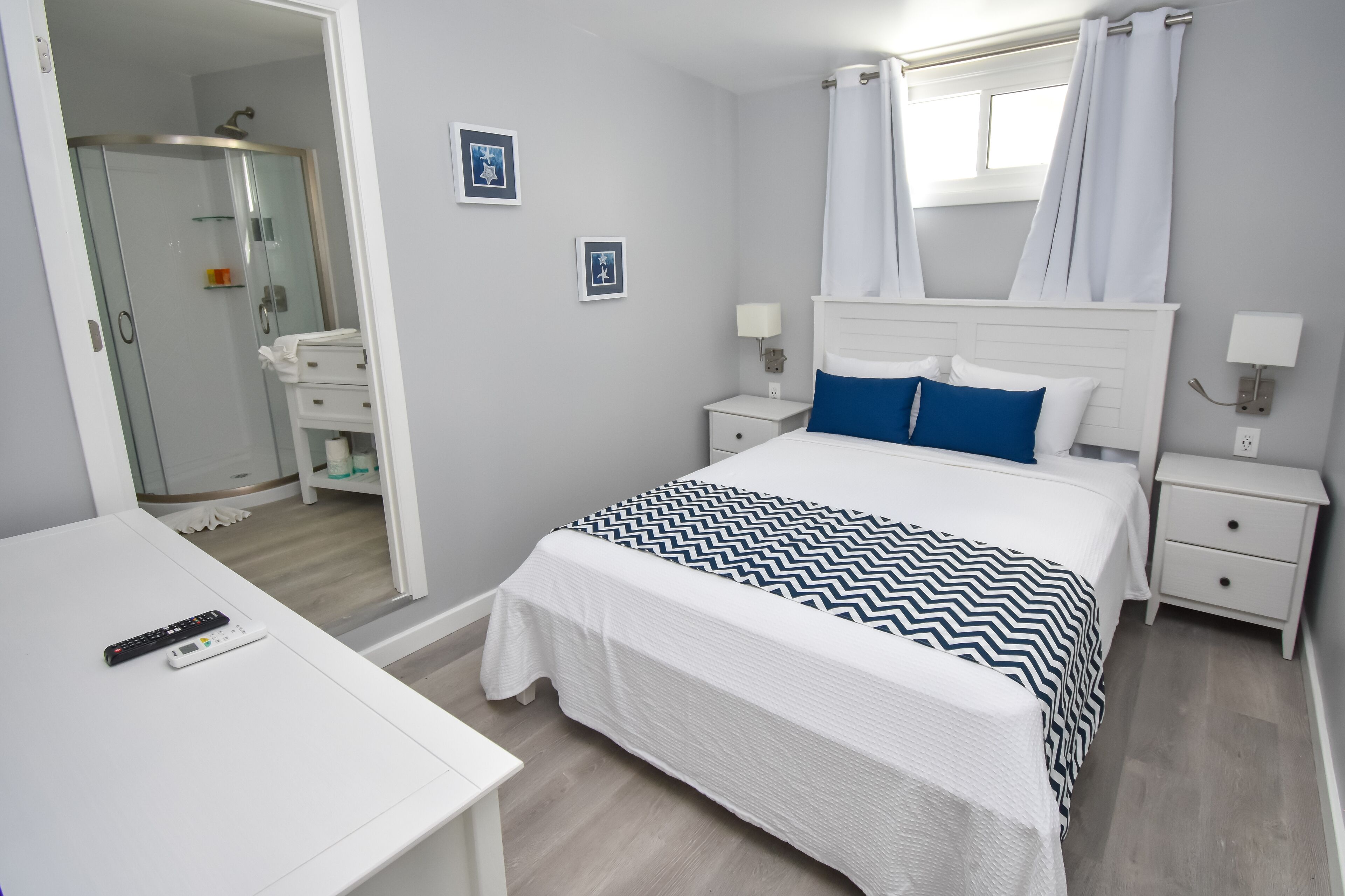A neatly arranged bedroom with a bed, bedside tables, a nightstand, a desk, and a bathroom visible through an open door.