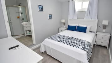 A neatly arranged bedroom with a bed, bedside tables, a nightstand, a desk, and a bathroom visible through an open door.