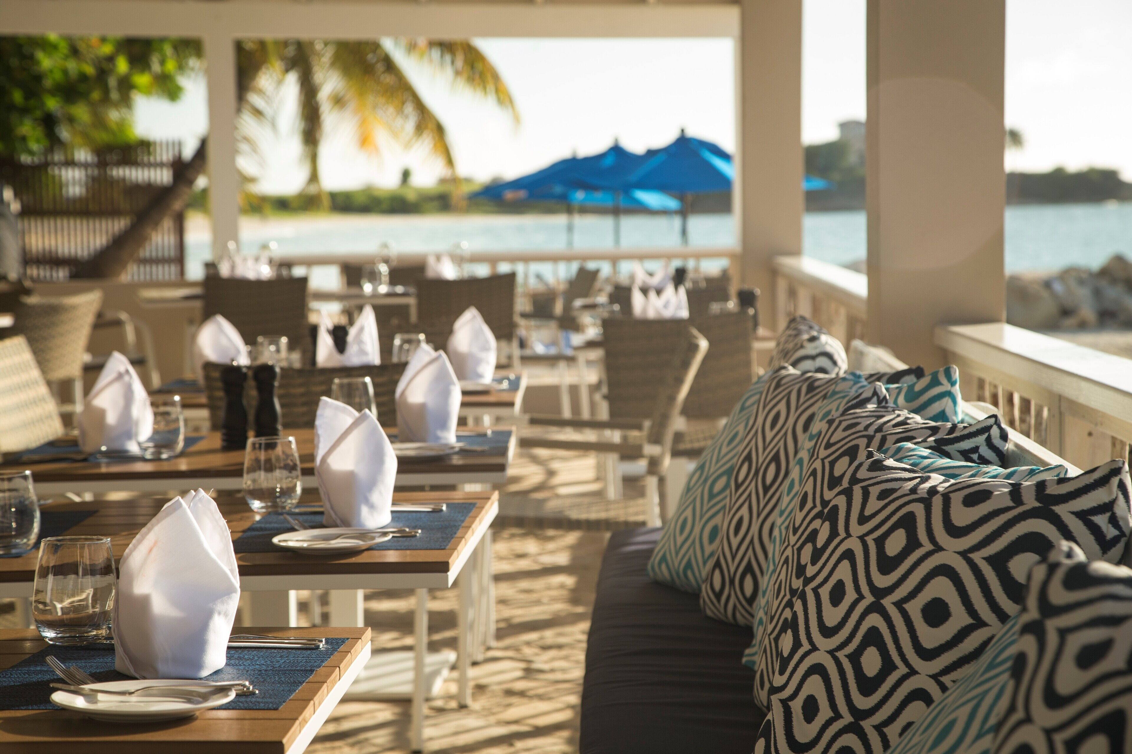 A beachfront restaurant with tables set for dining, overlooking the sea.