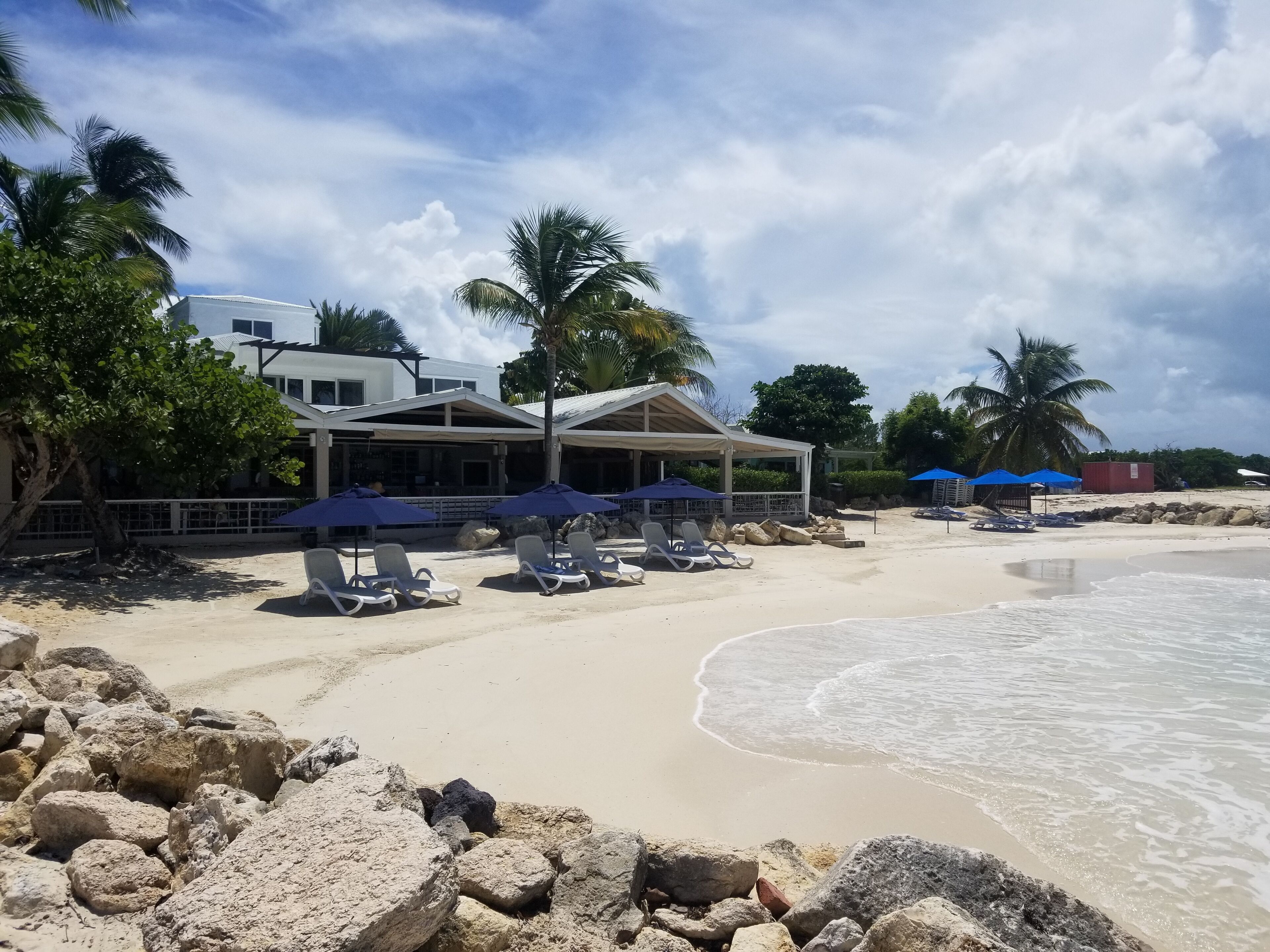 A beachside hotel with lounge chairs and umbrellas, a sandy beach, and palm trees.