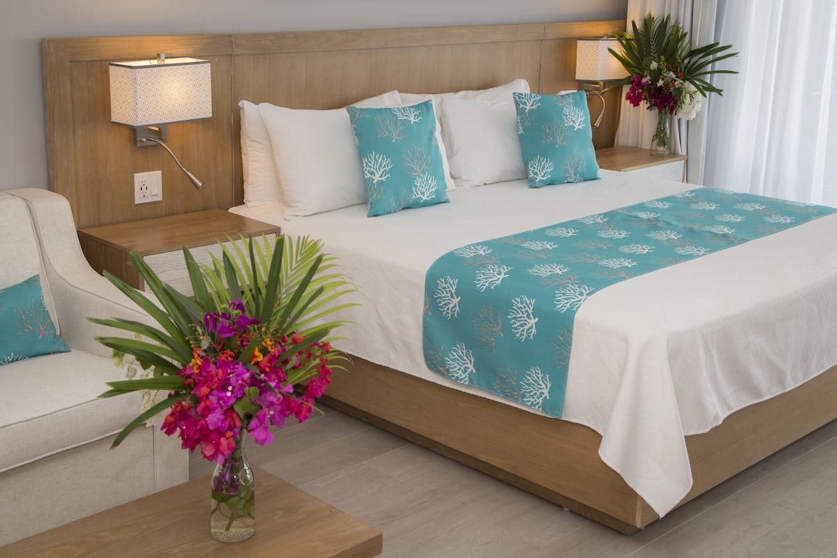 Une chambre d’hôtel avec un grand lit, deux tables de chevet, une petite table, une lampe et un vase avec des fleurs.