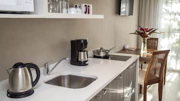 A modern kitchen with stainless steel appliances, a coffee maker, and a kettle. There is a dining area with a table and chairs, and a vase with flowers on the table.