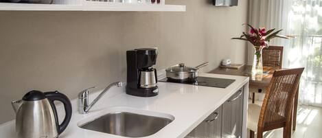 A modern kitchen with stainless steel appliances, a coffee maker, and a kettle. There is a dining area with a table and chairs, and a vase with flowers on the table.