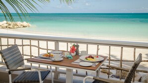 A table with plates of food and drinks, overlooking a beach with clear turquoise water. - Siboney Beach Club (St. John's)