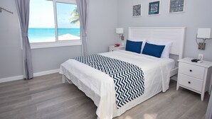 A bedroom with a bed, nightstands, a window with a view of the beach, and wall art. - Siboney Beach Club (St. John's)