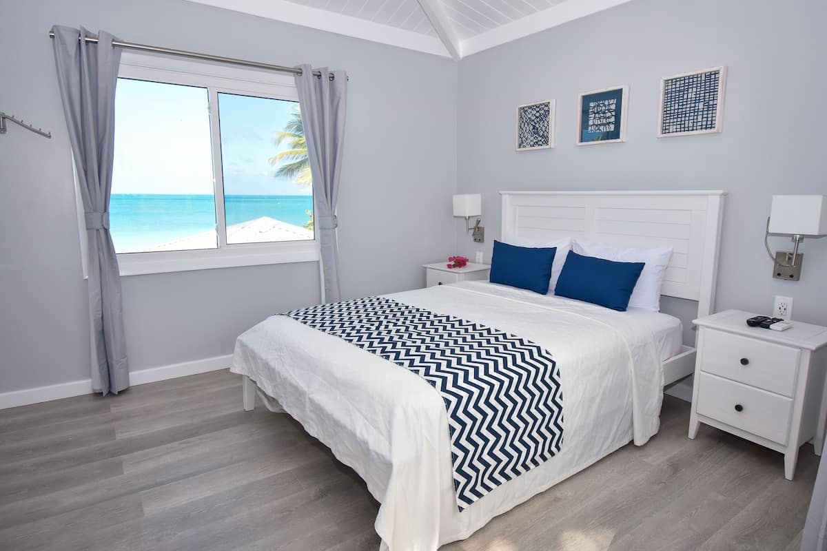 Une chambre à coucher avec un lit, des tables de chevet, une fenêtre donnant sur la plage et des œuvres d’art murales.