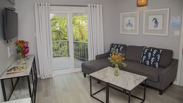 A living room with a grey sofa, a coffee table, a TV, and a balcony with curtains.