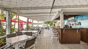 An outdoor bar area with wooden tables and chairs, red umbrellas, and a view of the sea. - Siboney Beach Club (St. John's)