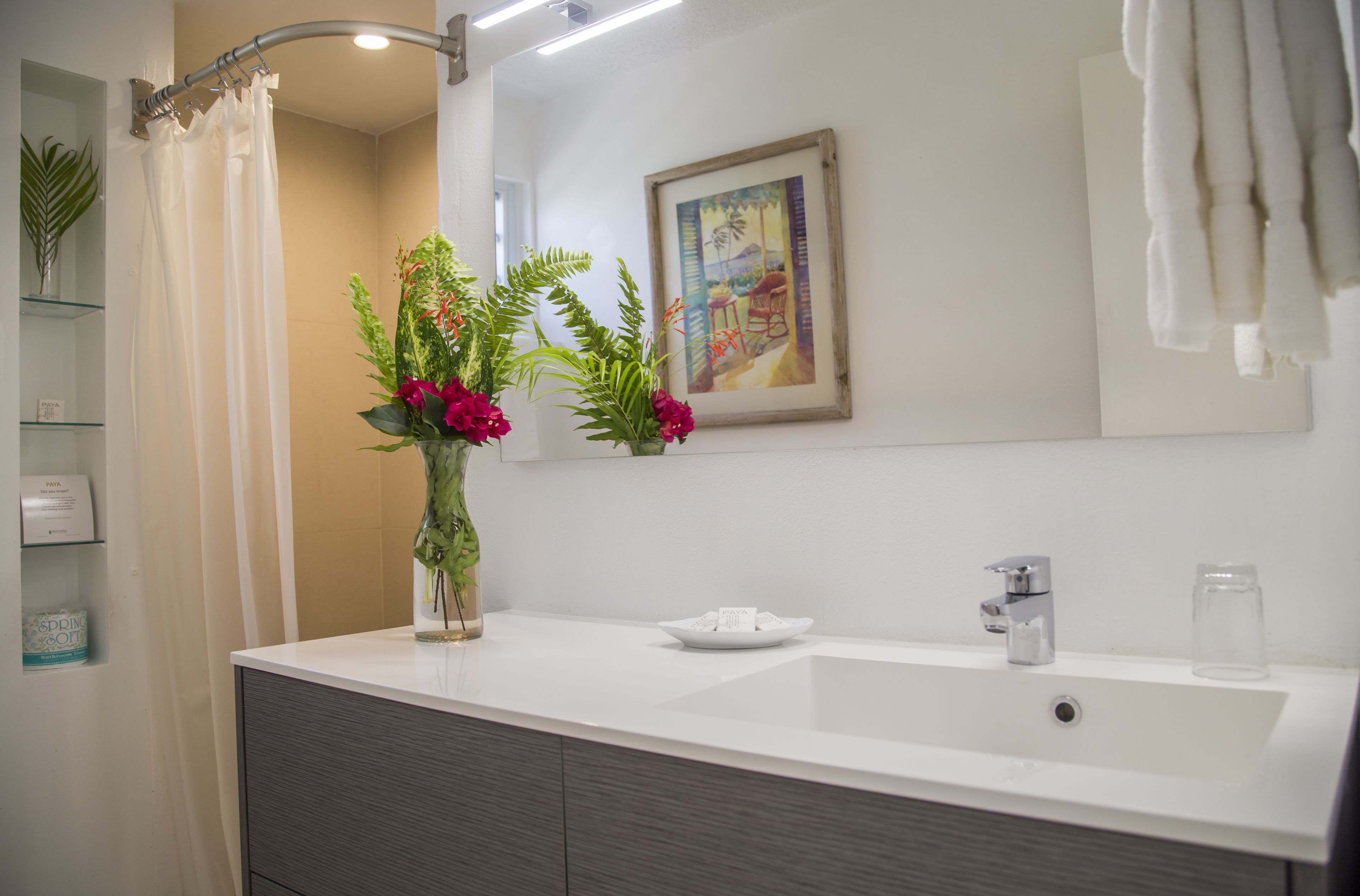 A modern bathroom with a white sink, a glass shower enclosure, and a framed painting on the wall.