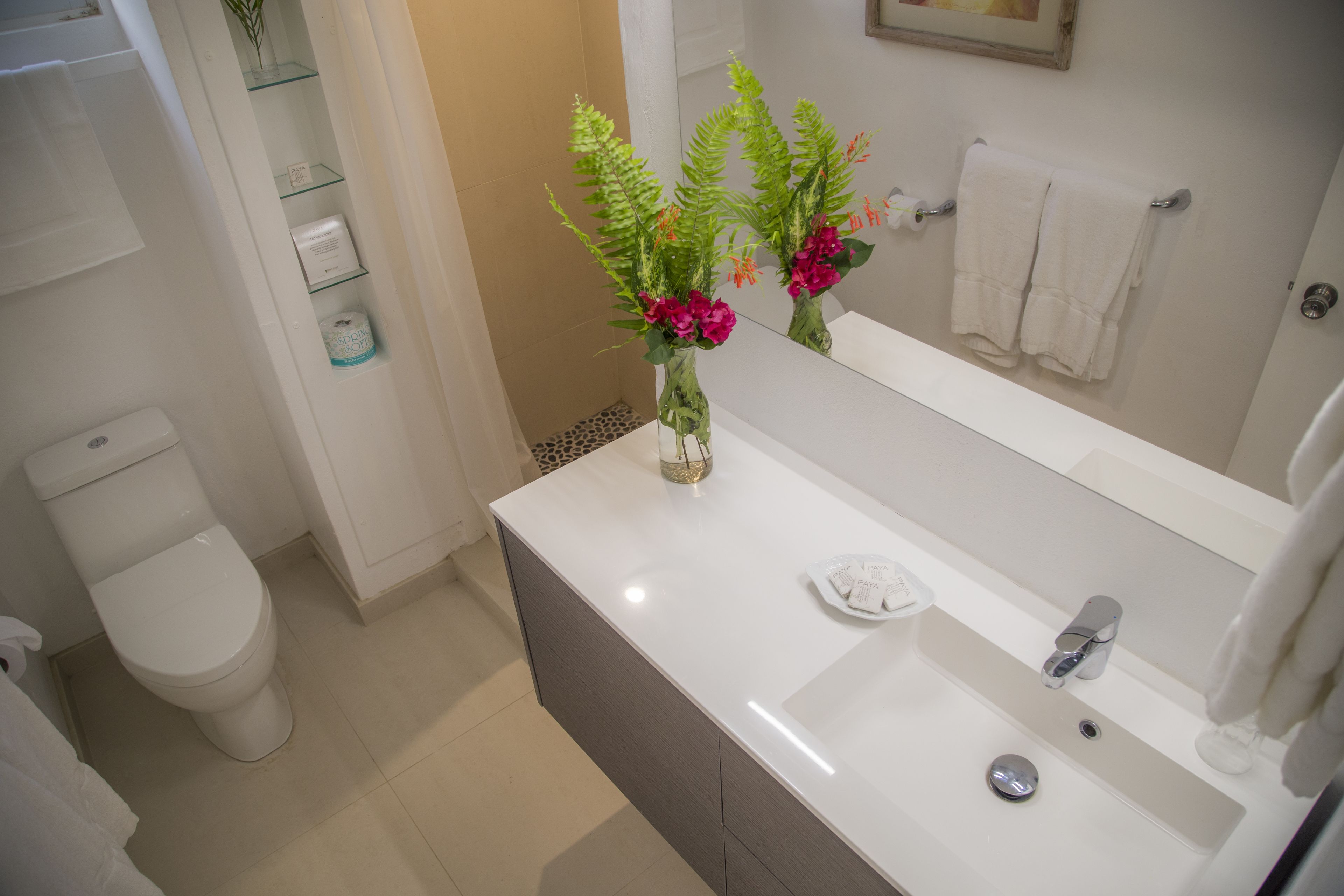 A bathroom with a white toilet, a sink with a mirror, and a vase with flowers.