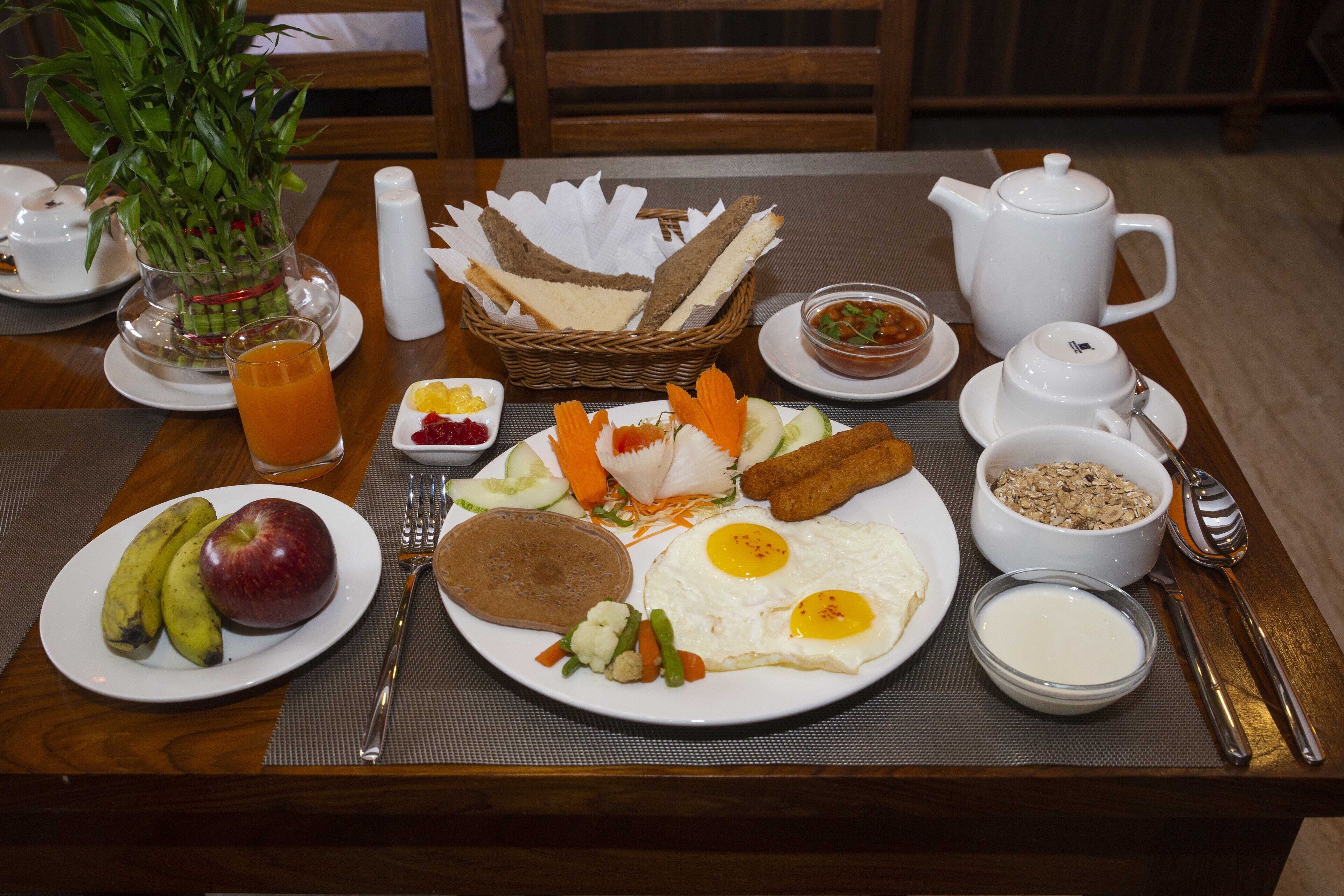 A breakfast table with plates of eggs, toast, fruit, and cereal.