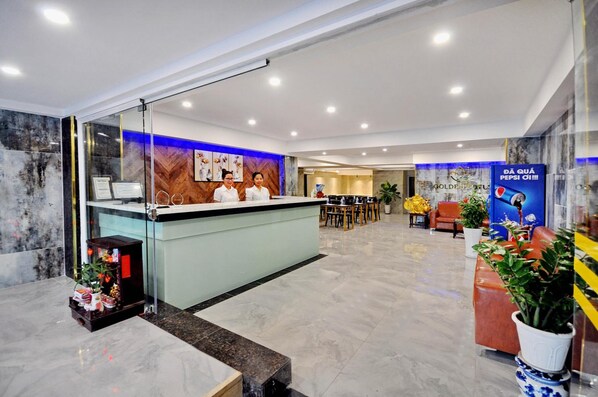 A hotel reception area with a glass partition, a reception desk, and a seating area with a sofa and chairs. - Golden Lotus Hotel (Nha Trang)