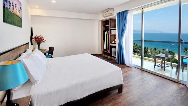 A hotel room with a large bed, a desk with a lamp, a wardrobe, and a balcony with a view of the sea. - Golden Lotus Hotel (Nha Trang)