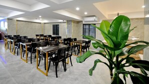 A spacious dining area with multiple tables and chairs, a large potted plant, and an air conditioning unit on the wall. - Golden Lotus Hotel (Nha Trang)