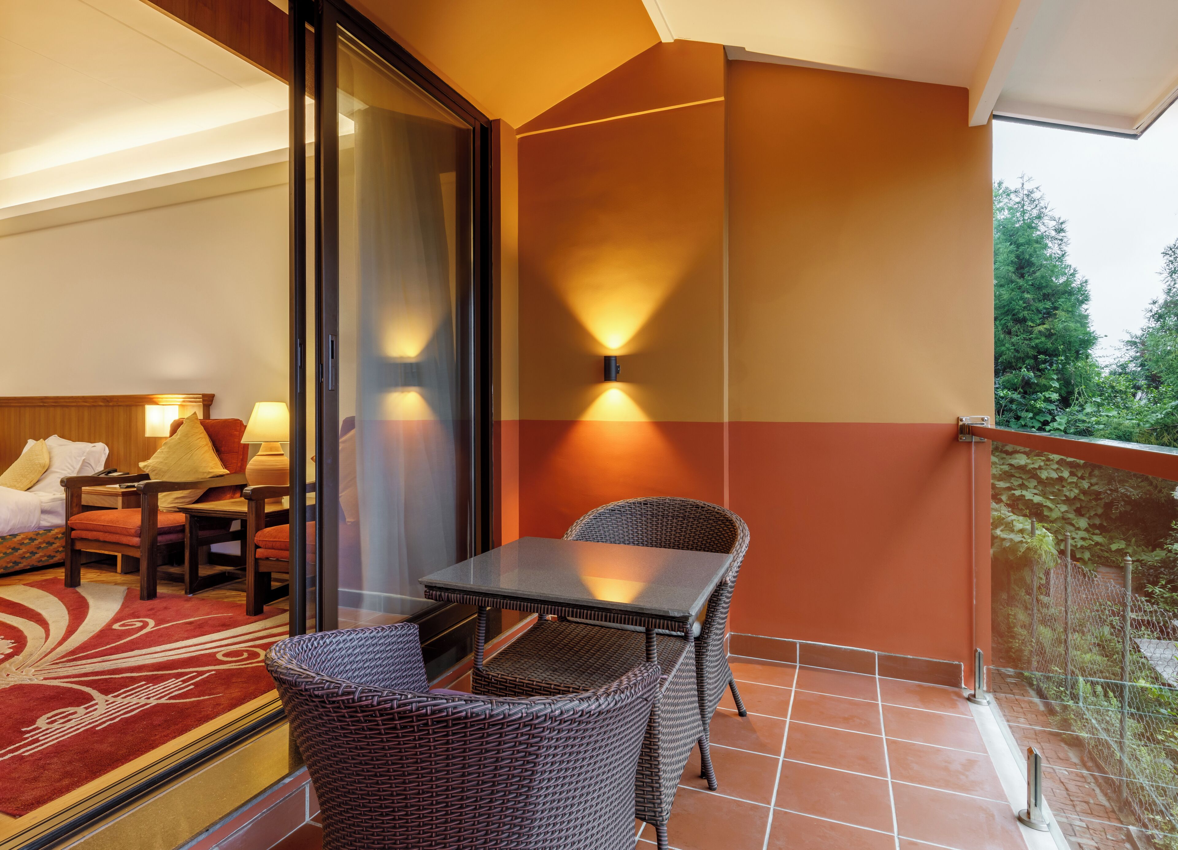 A balcony with wicker furniture, a table, and a red carpet.