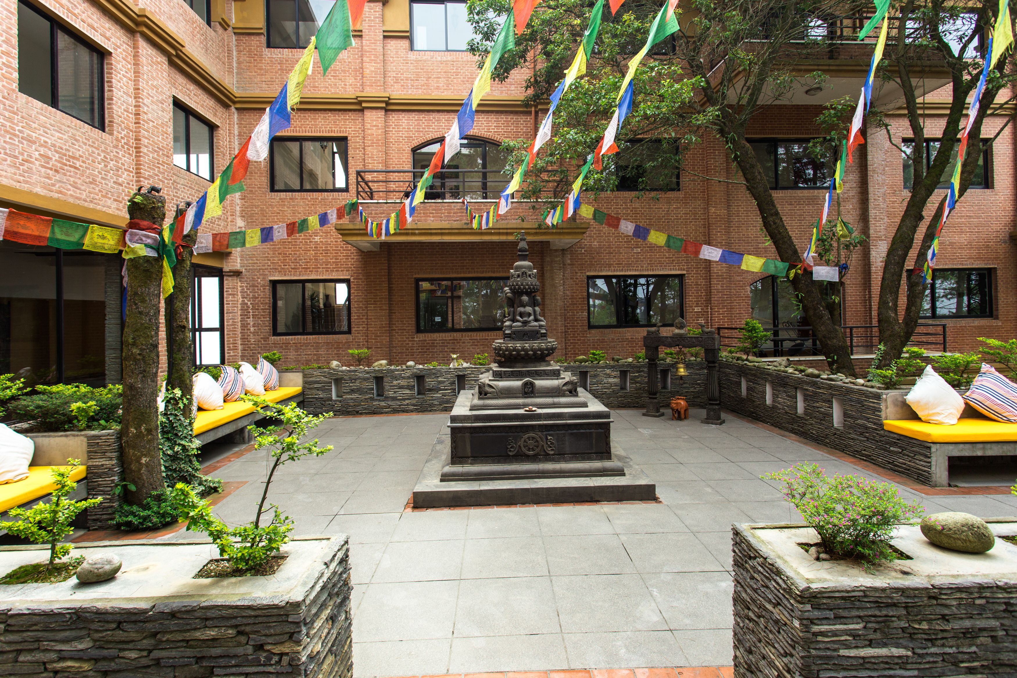 A courtyard with a central fountain, stone benches, and colorful flags.