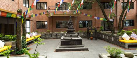 A courtyard with a central fountain, stone benches, and colorful flags.