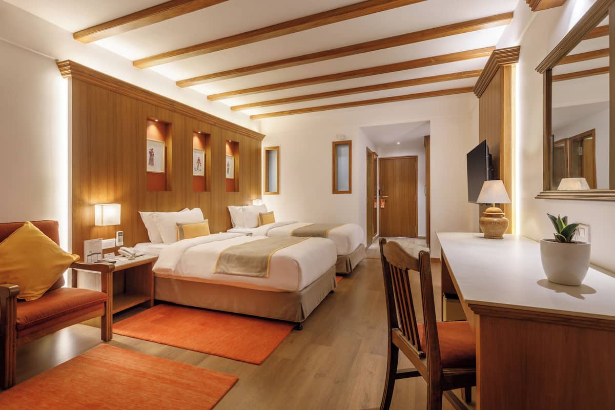 Une chambre d’hôtel avec deux lits, un bureau, une chaise, un canapé, une télévision et un grand miroir.