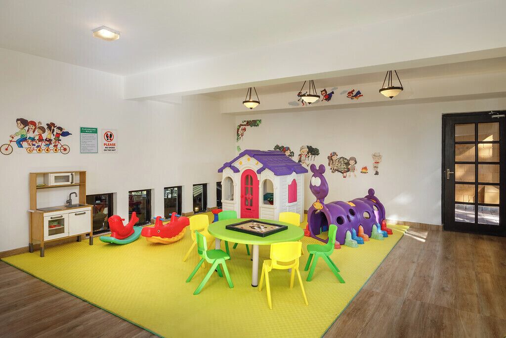 A children's playroom with a playhouse, colorful chairs, and a small kitchen area.