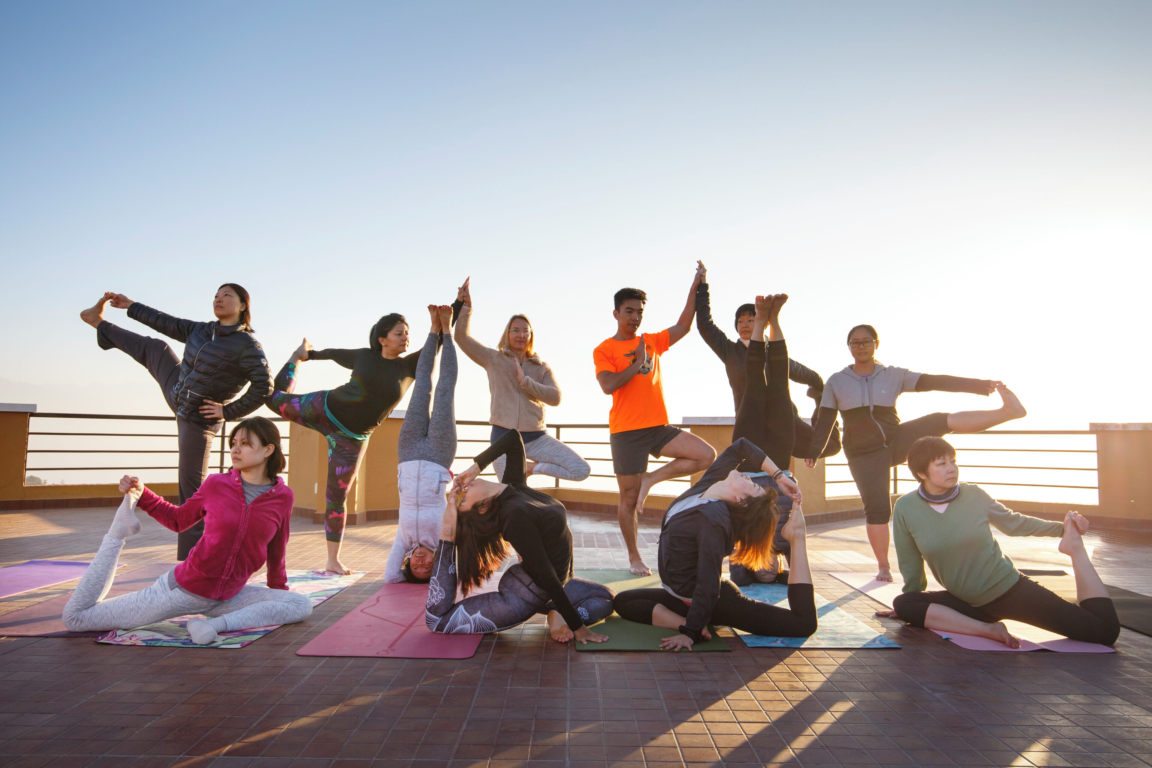 A group of people performing yoga on mats outdoors with a clear sky in the background.