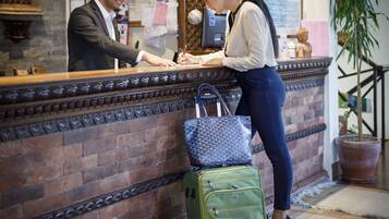 A reception desk with a man and a woman interacting, a green suitcase, and a blue patterned bag.