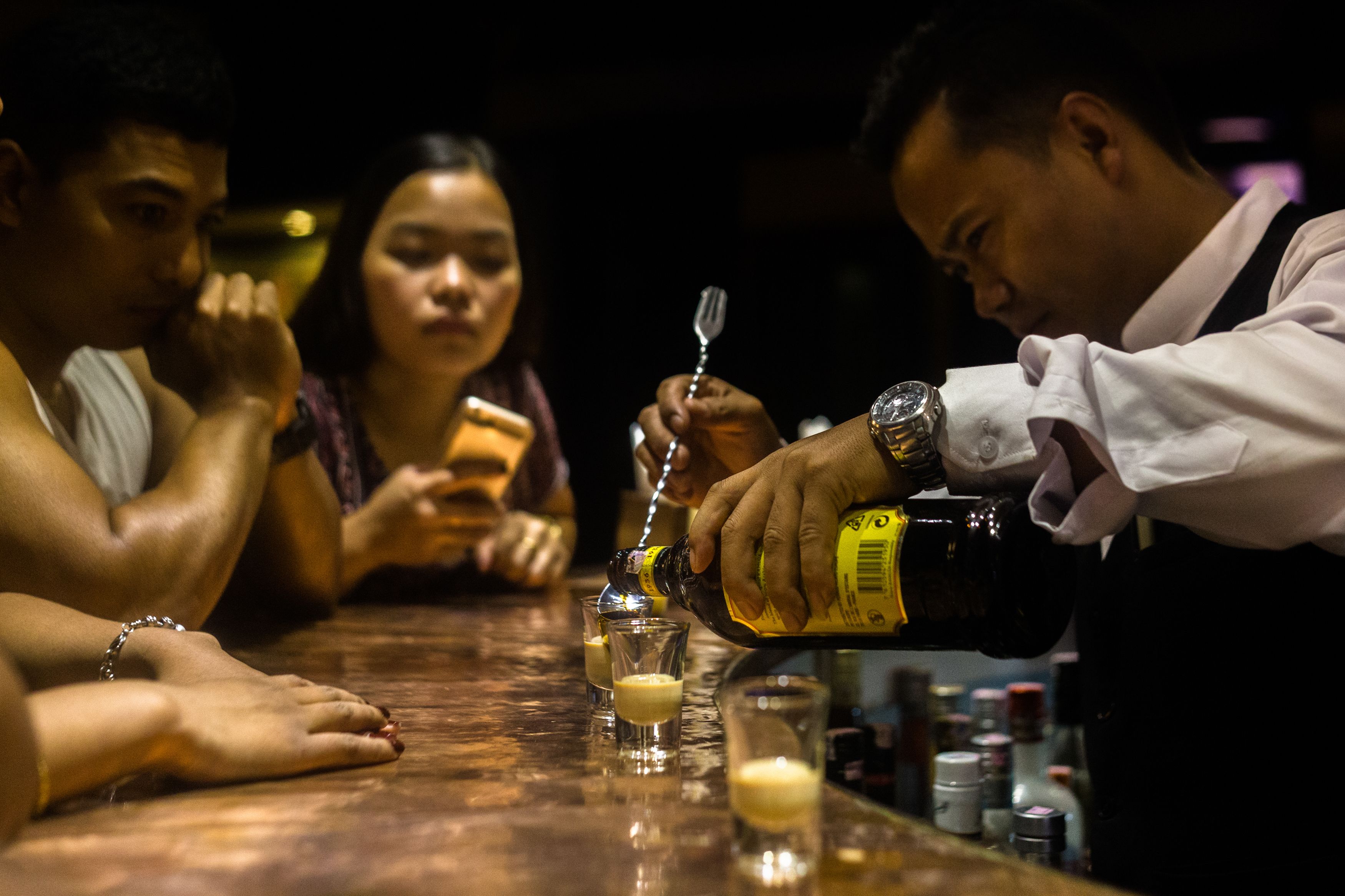 A bar setting with a person pouring a drink into a glass.
