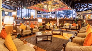 A spacious lobby with multiple seating areas, a high ceiling with exposed beams, and large windows providing natural light.