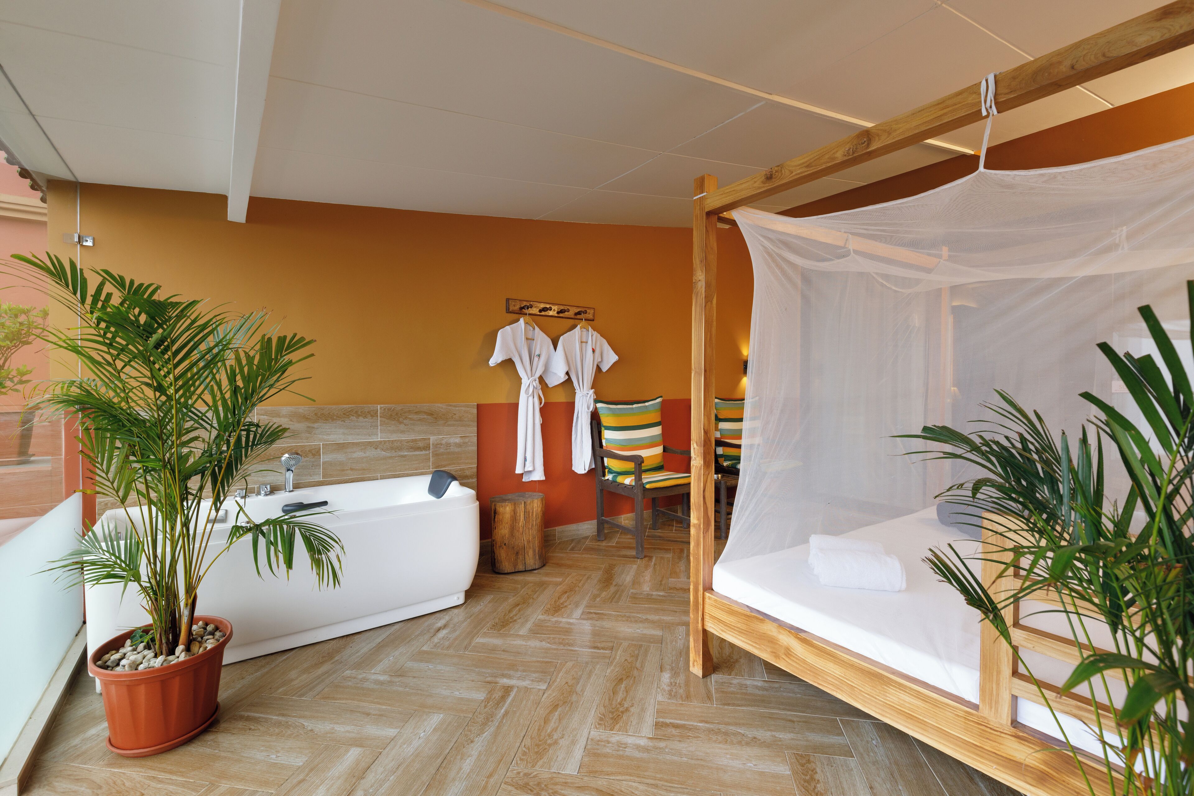 A room with a large bathtub, a canopy bed, and two potted plants.