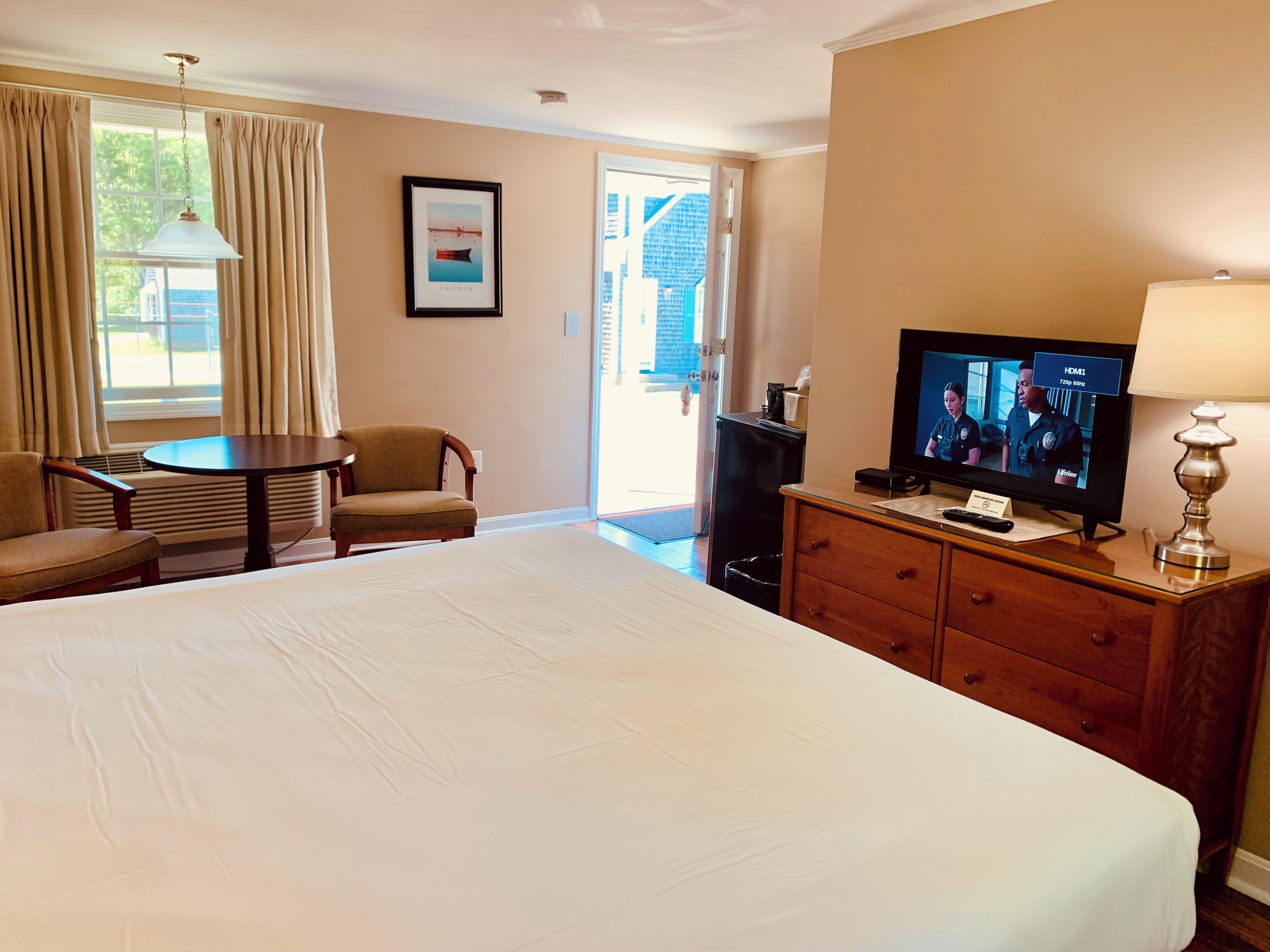Ein Hotelzimmer mit einem großen Bett, einem Fernseher, einem Schreibtisch, einem Stuhl und einem Fenster mit Vorhängen.